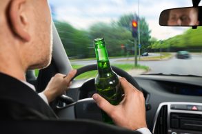 Motorista com garrafa de cerveja na mão bebendo ao dirigir