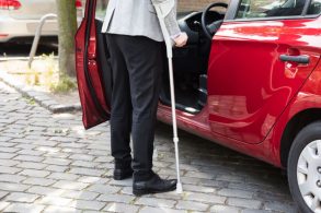 homem de muleta entrando em carro vermelho