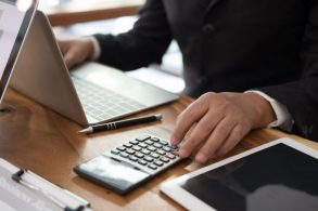 Mão masculina calculando e registrando informações no computador