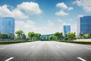 imagem mostra uma rua pavimentada sem pessoas e sem carros com predios ao redor e o ceu azul acima