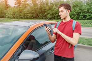 jovem com celular na mao com aplicativo de carsharing aberto representando carro multiplo