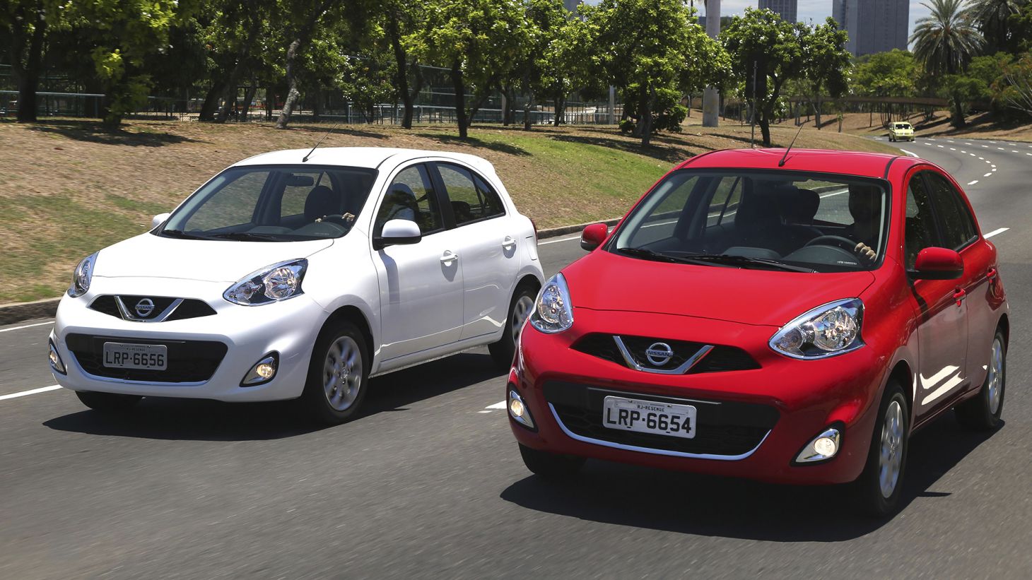 Dois Nissan March juntos; um na cor vermelha e outro na cor branca com a dianteira em detalhe em movimento na estrada