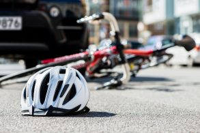 capacete e bicicleta caidos no chao com carro atras indicando acidente de transito