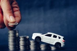 mão feminina empilha moedas abaixo de carrinho de brinquedo simulando aumento do preço dos carros