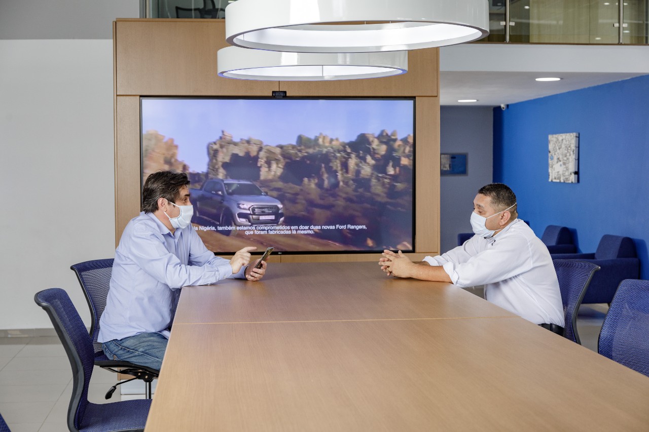 dois homens de camisa social e mascara em sala de reuniao da ford