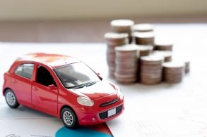 carrinho de brinquedo vermelho em frente a pilha de moedas representando impostos ligados a veiculos como ipva