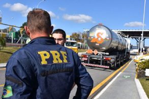 policial federal conversa com homem em estrada com caminhao ao fundo