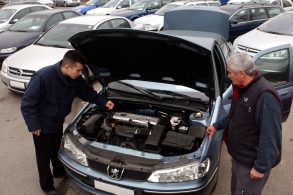 dois homens verificam carro usado com capo aberto