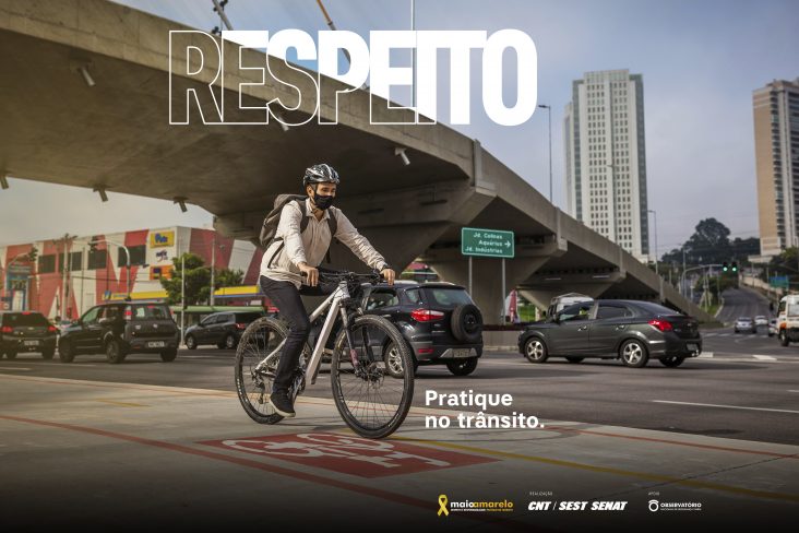 ciclista de capacete pedala em ciclovia com transito em segundo plano