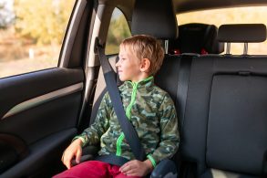 menino com blusa de frio sentado no banco traseiro do carro com booster