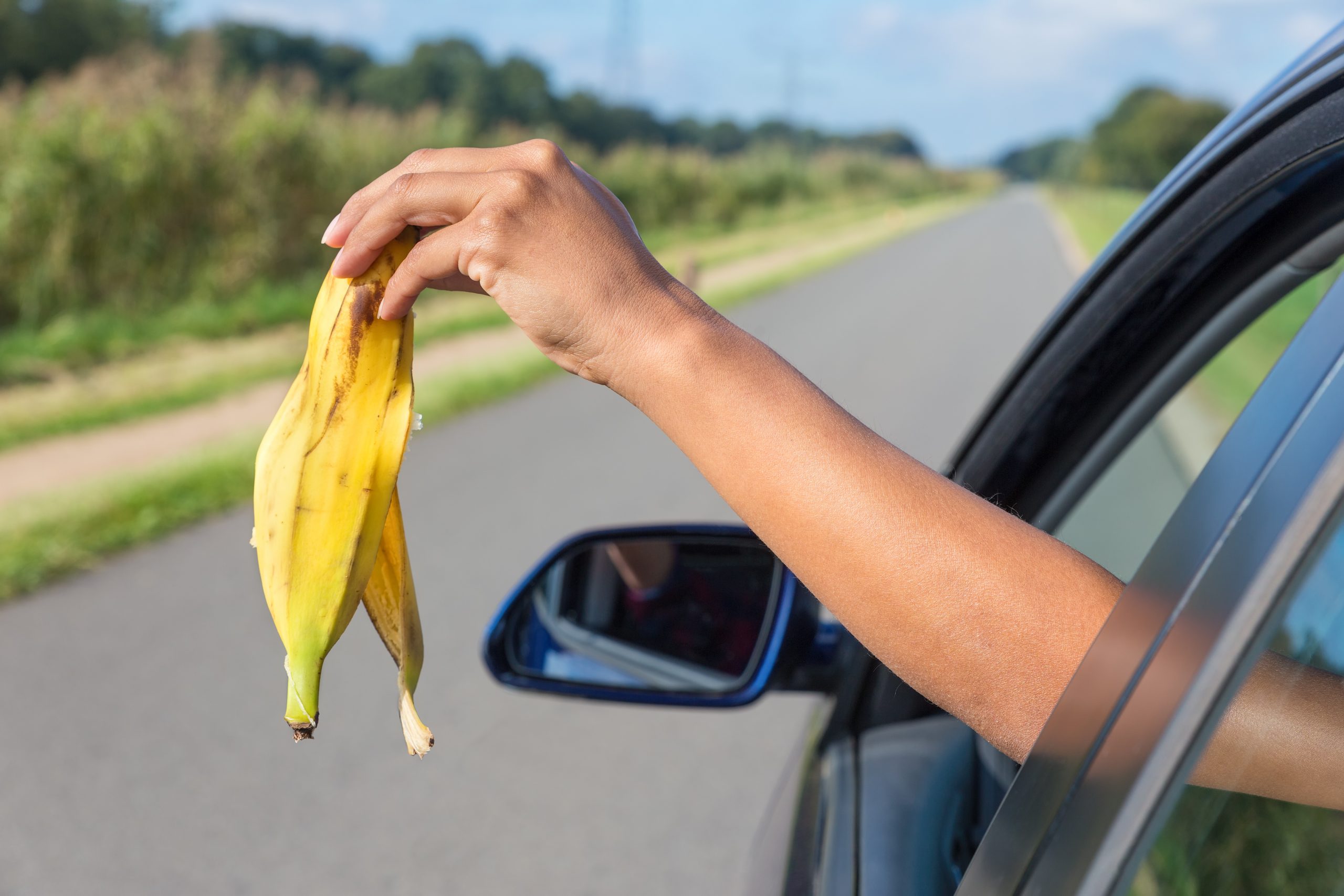 mao feminina jogando casca de banana como lixo pela janela do carro
