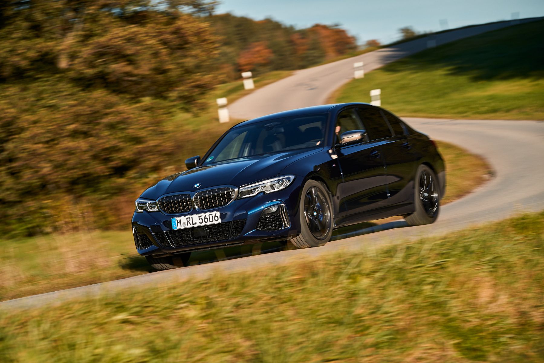 bmw m340i xdrive azul escuro frente em movimento fazendo curva em rodovia simples