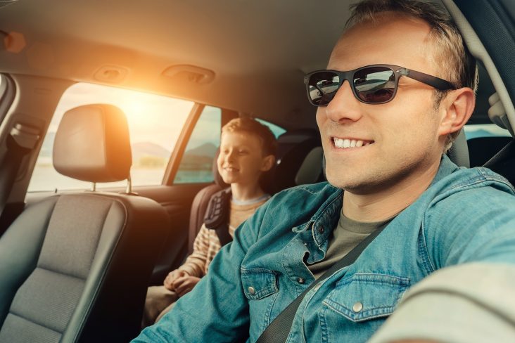 pai dirigindo carro com filho sentado em cadeirinha no banco traseiro