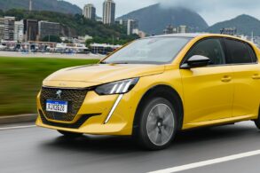 peugeot e 208 gt amarelo frente em movimento cidade ao fundo