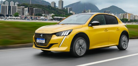 peugeot e 208 gt amarelo frente em movimento cidade ao fundo