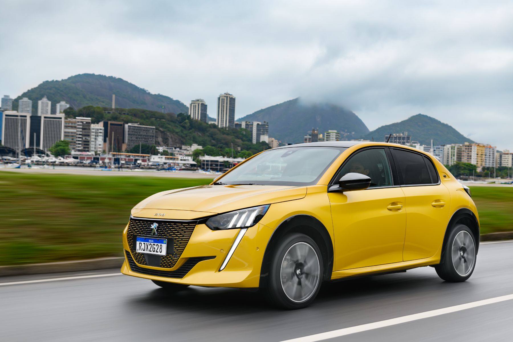 peugeot-e-208-gt-amarelo-frente-em-movimento-cidade-ao-fundo.jpeg