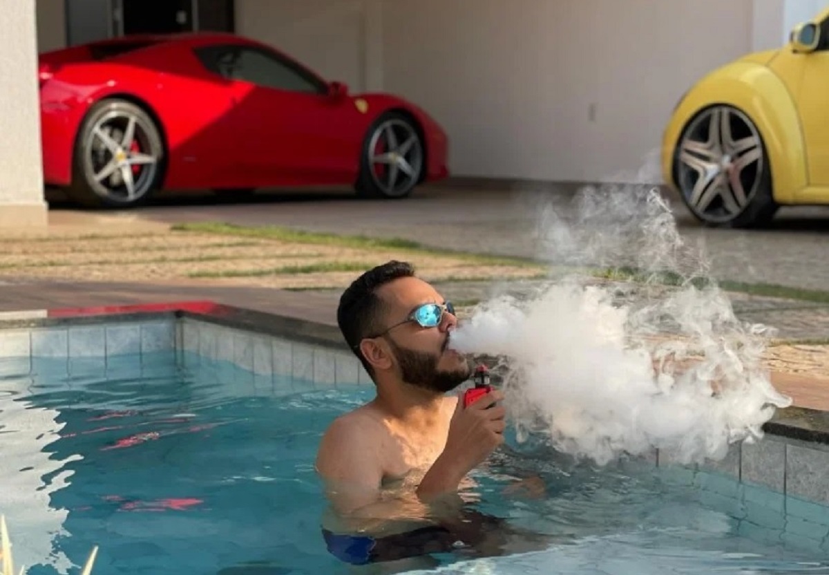 youtuber klebim fumando em piscina com ferrari vermelha e new beetle amarelo ao fundo