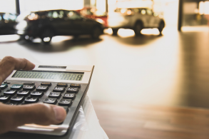 mao masculina em cima de calculadora com carros ao fundo indicando contas consorcio carro