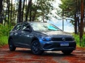 volkswagen polo track 2023 cinza platinum frente parado em estrada de interior com arvores ao fundo e folhas caidas na pista 2