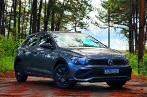 volkswagen polo track 2023 cinza platinum frente parado em estrada de interior com arvores ao fundo e folhas caidas na pista 2