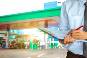 shutterstock homem com prancheta em primeiro plano com posto de gasolina ao fundo fiscalizacao