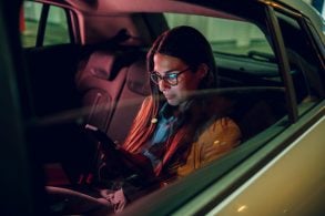 mulher jovem de oculos com celular nas maos sentada banco traseiro de carro uber app shutterstock