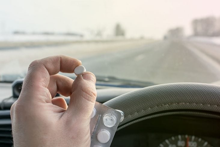 shutterstock motorista segurando cartela e comprimido de remédios enquanto dirige