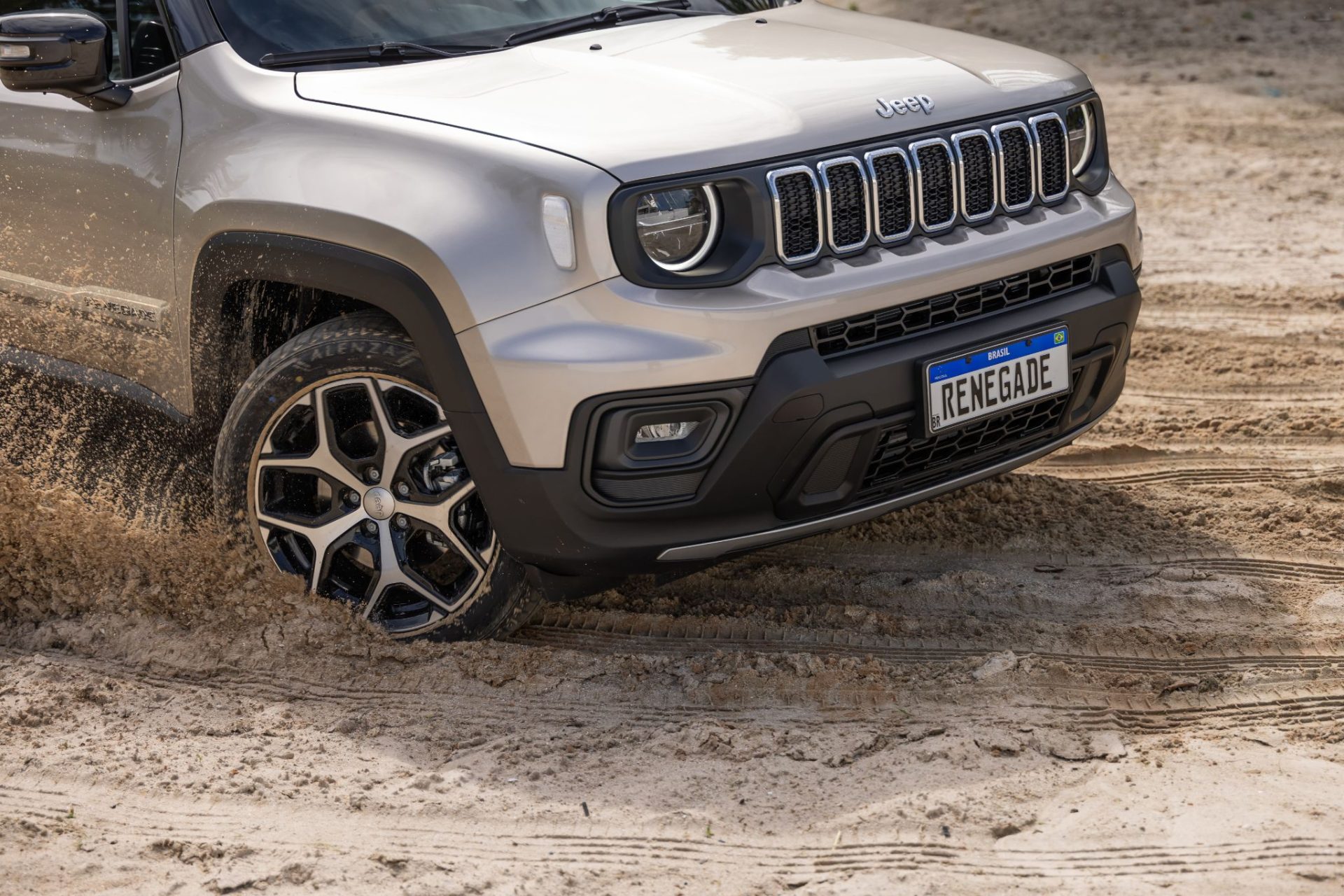 Jeep Renegade Sahara 2025 slash gold fazendo curva em areia dianteira