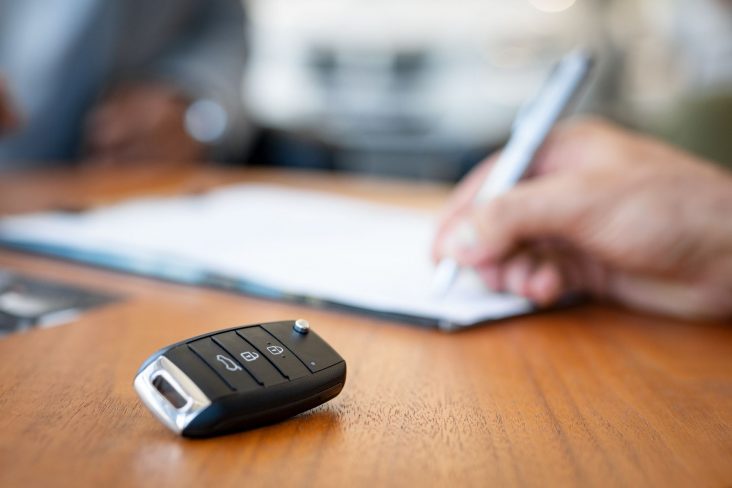 chave de carro em cima da mesa com mao assinando contrato de carro por assinatura ao fundo