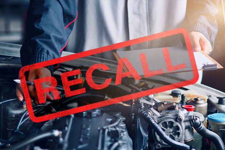 recall escrito em primeiro plano mecanico com prancheta fazendo inspeção em motor do carro em segundo plano