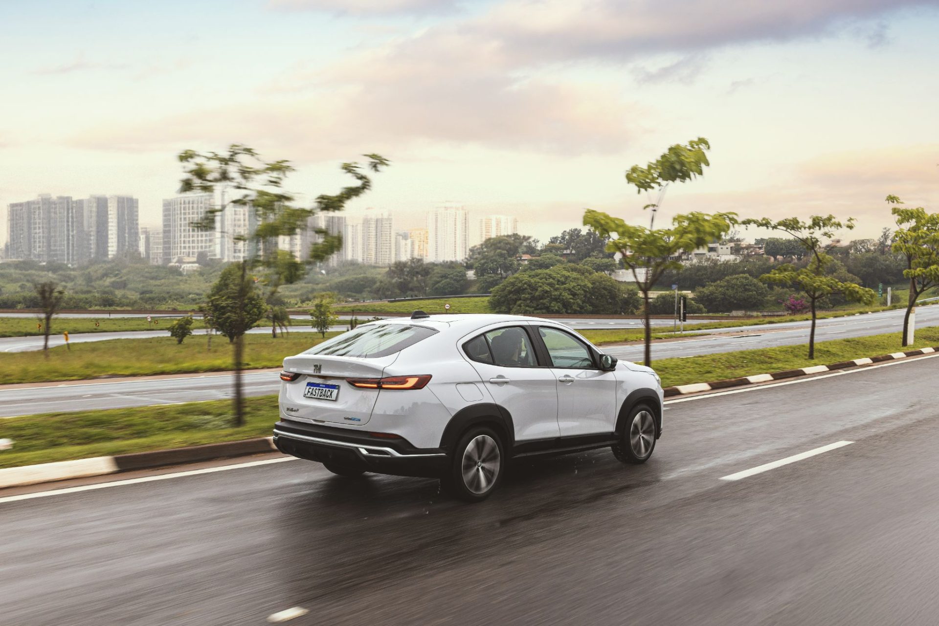 Fiat Fastback Audace Hybrid 2025 Branco Banchisa traseira em movimento em avenida molhada