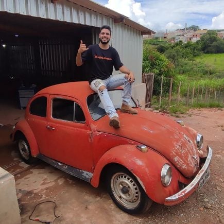 Tiu Luquinha sentado em cima de fusca vermelho que foi base do projeto