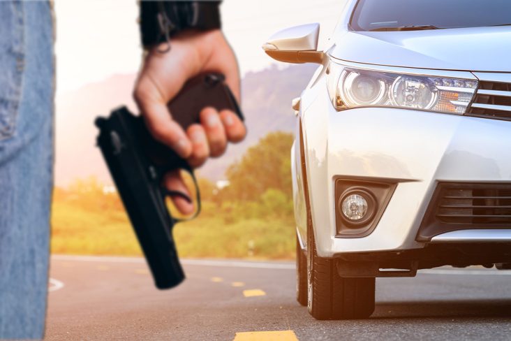 Um homem segurando uma arma e ao fundo um carro