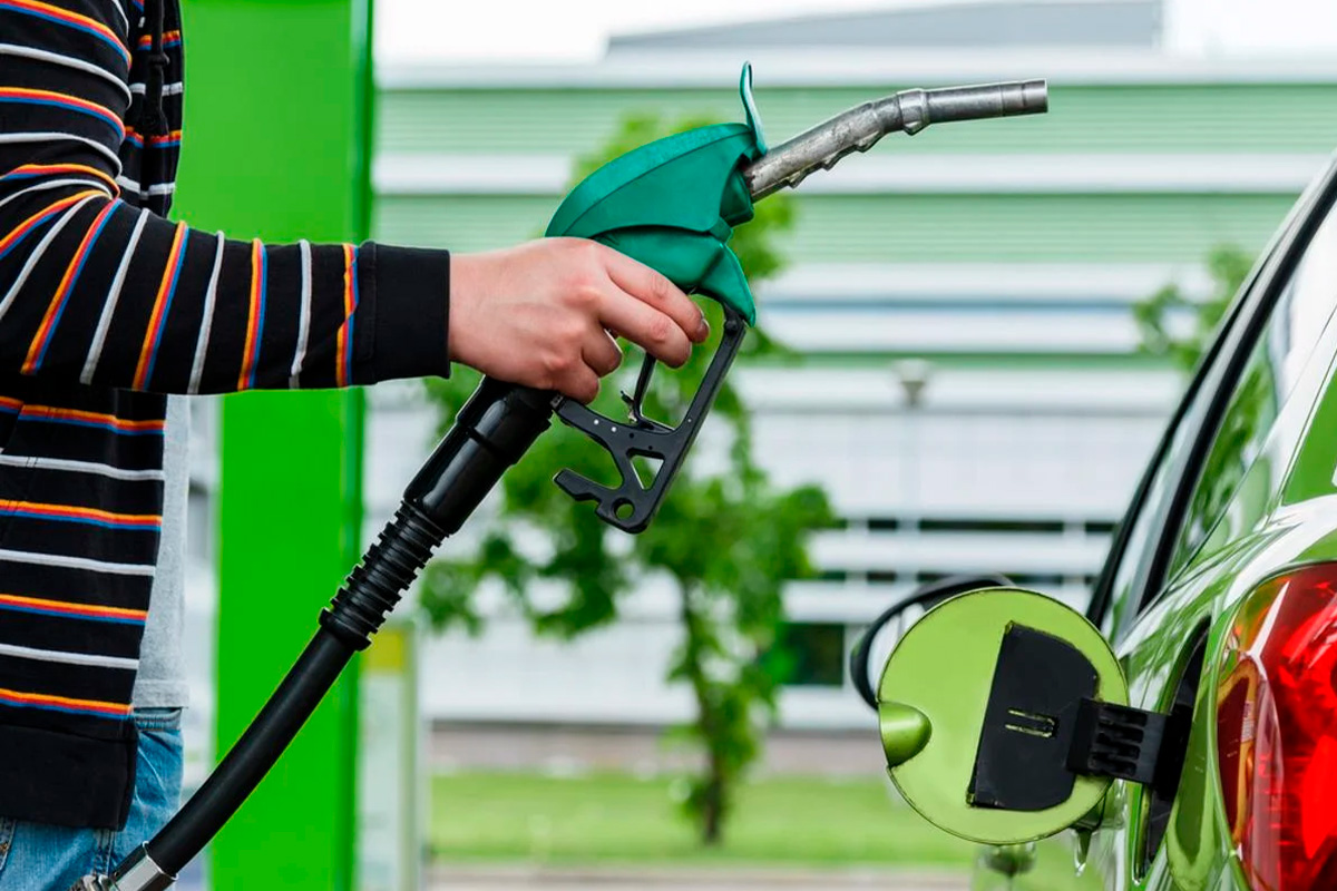 Homem segura a bomba de combustível verde com o carro flex parado no posto de gasolina.