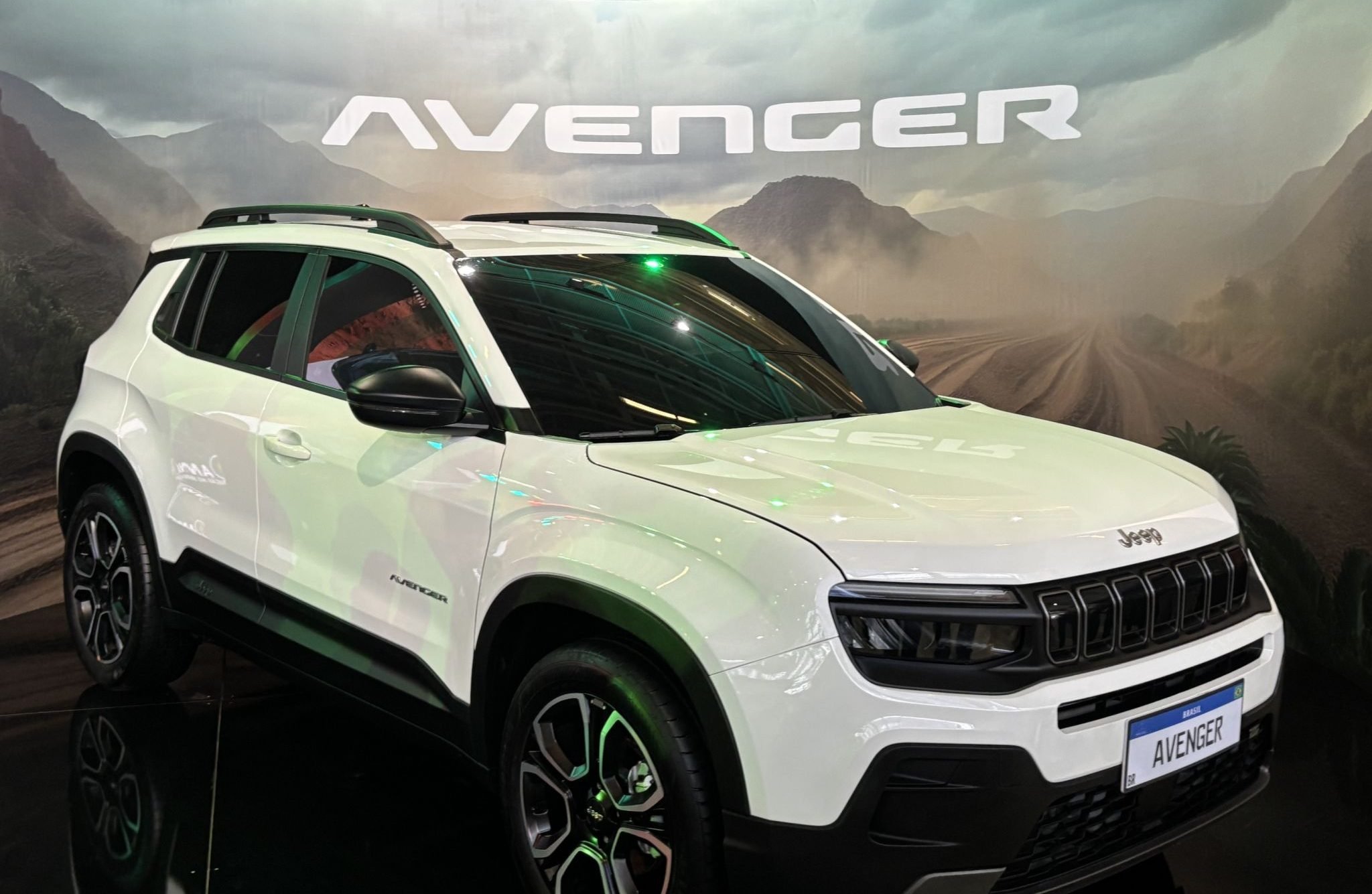 Jeep Avenger branco frente e lateral com banner atrás escrito o nome do veículo Jeep Avenger branco frente e lateral com banner atrás escrito o nome do veículo