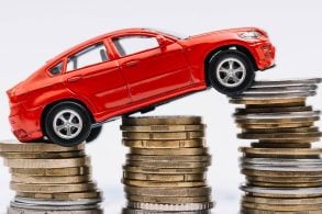 Carro de brinquedo em cima de três pilhas crescentes de moedas