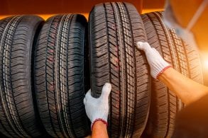 UMA PESSOA COM MÁSCARA E LUVAS PEGA UM PNEU NOVO NA PRATELEIRA DE PNEUS