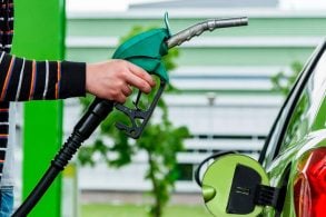 Homem segura a bomba de combustível verde com o carro parado no posto de gasolina.