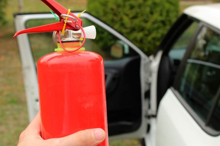 motorista segurando extintor incendio com carro automovel ao fundo