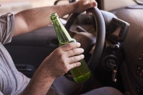 garrafa de cerveja nas maos de um homem dirigindo o carro durante o dia