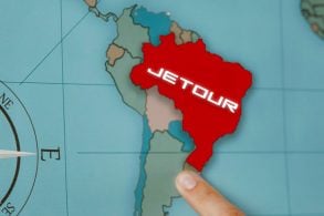 Mapa cartográfico da América do Sul e um dedo aponta para o Brasil em vermelho com símbolo da Jetour.