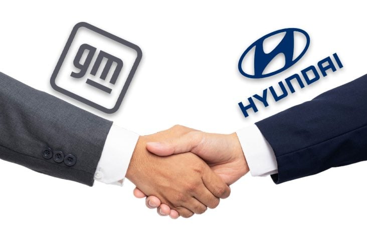 Duas mãos masculinas se cumprimentam do lado esquerdo ao fundo a logo da GM e na direita a Logo da Hyundai.