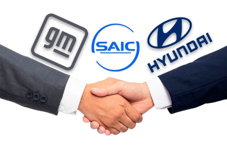 Duas mãos masculinas se cumprimentam do lado esquerdo ao fundo a logo da GM e na direita a Logo da Hyundai ao meio logo da SAIC.