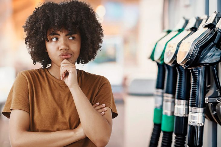 Mulher negra olha em dúvida para as pistolas de combustivel
