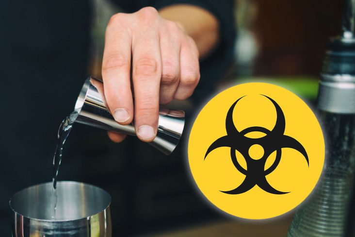 Símbolo de risco biológico, uma barman preparando um drink de destilado com foco em sua mão.