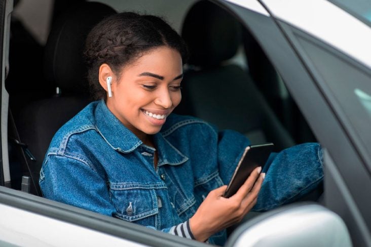 shutterstock motorista com fones de ouvido sem fio e usando celular