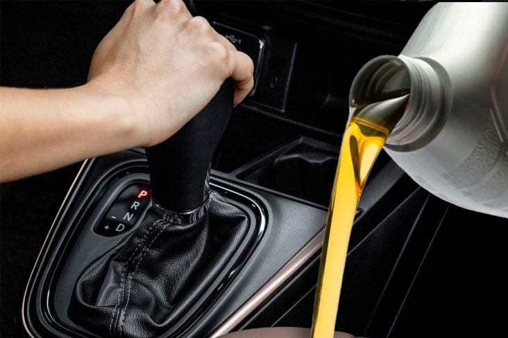 Ao fundo motorista muda de posição o câmbio automático. A frente um frasco de óleo.
