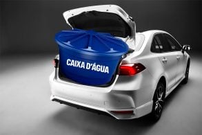 Toyota Corolla GR Sport 2025 branco traseira com porta-malas aberto, caixa d'água azul ocupando o espaço interno do porta-malas