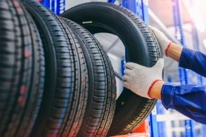 Mão de homem pegando um Pneu na prateleira junto a outros pneus