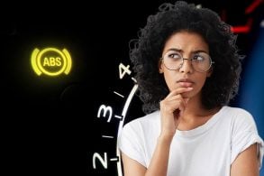 Mulher negra com blusa branca e óculos olha para o lado com a mão no queixo a sua esquerda símbolo do freio ABS